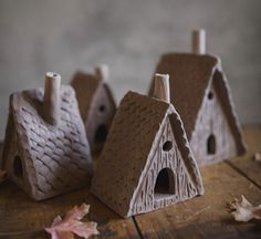 three small houses made out of clay sitting on top of a wooden table next to leaves