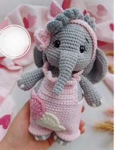 a crocheted stuffed elephant in a pink and gray dress is held by someone's hand