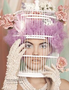 a woman holding a bird cage over her face with flowers in it and wearing gloves