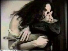 a woman with long hair holding a cat in her arms and looking at the camera