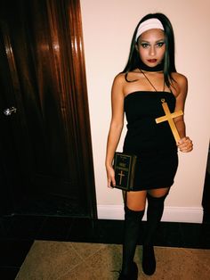 a woman in a black dress and headband holding a cross on her chest, standing next to a door