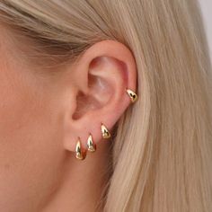 a woman with blonde hair wearing three gold ear climbrs in front of her ear