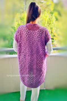 a woman wearing a purple knitted shawl looking out over a balcony at greenery