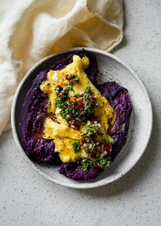 a white plate topped with purple potatoes covered in cheese and toppings next to a napkin