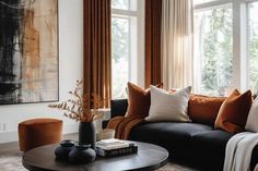 a living room filled with lots of furniture and large windows covered in orange drapes