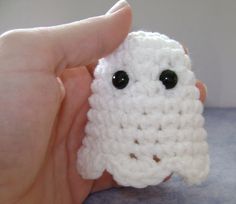 a hand holding a small white crocheted object with eyes on it's face