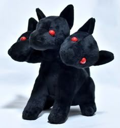 two black stuffed animals sitting next to each other on a white surface with red eyes