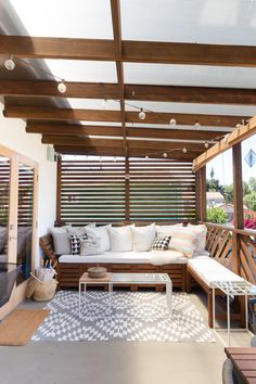 an outdoor living area with white furniture and wood slats on the ceiling, along with large windows