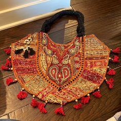 a red and gold purse with tassels sitting on top of a wooden floor