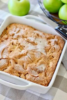 an apple pie in a white dish next to green apples