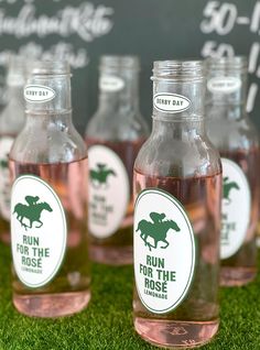 four bottles of run for the rose water are sitting on green grass in front of a chalkboard