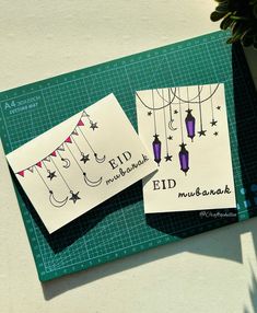 two cards with the words eid mubarak written on them next to a potted plant