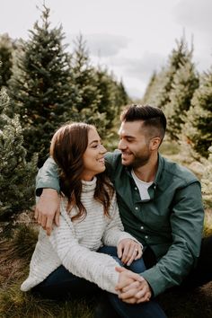 a man and woman sitting on the ground in front of christmas trees smiling at each other