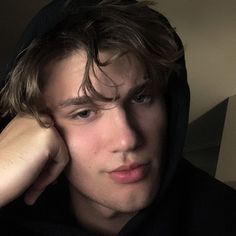 a young man wearing a black hoodie and holding his hand to his face while looking at the camera