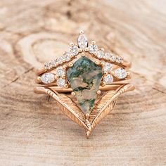 a gold ring with a green and white stone surrounded by diamonds on top of a piece of wood