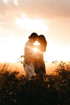 a man and woman kissing in front of the sun with their arms around each other