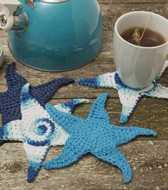 two crocheted starfish coasters next to a teapot on a wooden table