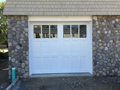 a white garage with two windows and rocks on the side