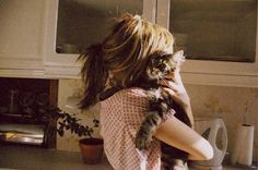 a woman holding a cat in her arms while standing next to a stove top oven