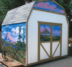 a small white shed with a mountain scene painted on it's side and windows