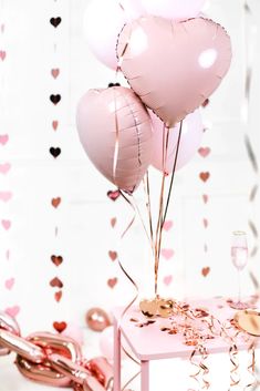 pink balloons and confetti on a table with hearts hanging from the wall behind them