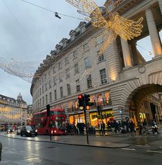 a red double decker bus driving down a street next to tall buildings covered in christmas lights