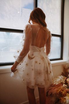 a woman standing in front of a window wearing a white dress with stars on it