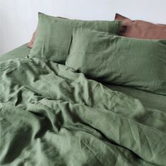 an unmade bed with green linens and brown pillow cases on top of it