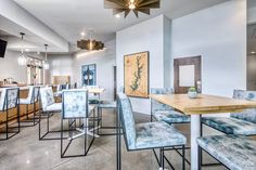 an empty restaurant with blue chairs and wooden tables in front of a bar area that also has seating for people