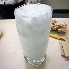 a glass filled with ice sitting on top of a table next to a yellow pencil