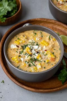 a bowl of corn chowee on a wooden plate with lime wedges and cilantro