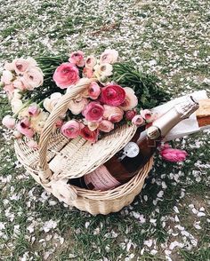 a wicker basket filled with bottles and flowers on top of snow covered grass next to a bottle of wine