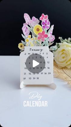 a white calendar with flowers on it next to a bouquet of yellow and pink flowers