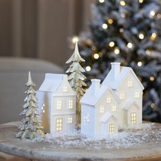 a small white house sitting on top of a wooden table next to a christmas tree