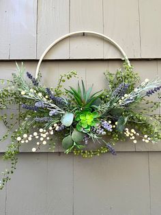 a wreath with flowers and greenery hanging on the side of a building in front of a wall