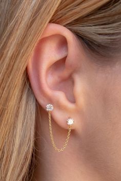 a woman's ear is shown with a gold chain and two small white stones