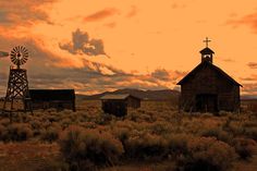 two old wooden buildings sitting in the middle of a field with a windmill on top