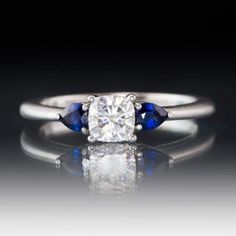 a diamond and blue sapphire ring on a reflective surface