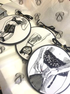 three hand embroidered plates with black and white images on them, one is holding a woman's bra