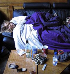 a woman laying on a couch covered in blankets and other items next to a coffee table