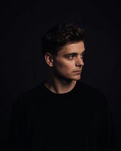 a man in black shirt looking off to the side with his eyes wide open and dark background