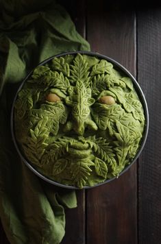 a green face made out of leaves on top of a wooden table next to a cloth