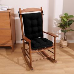 a wooden rocking chair with black cushions in a room