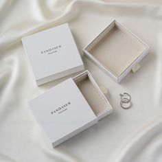 two white boxes with wedding rings sitting on a bed