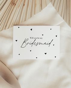 a card that says will you be my bridesmaid? on top of some white sheets