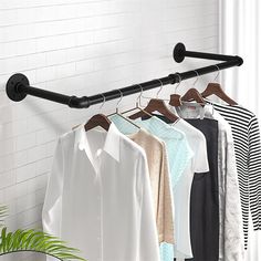 clothes hanging on rail in room with white brick wall and potted plant next to it