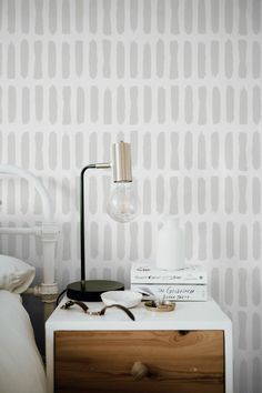 a nightstand with two books and a lamp on it next to a wallpapered bedroom