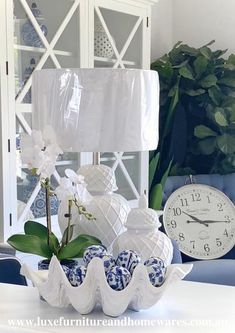 a white clock sitting on top of a table next to a blue and white vase