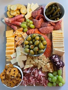 an assortment of cheeses, crackers, and olives on a wooden platter