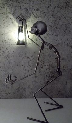 a metal sculpture holding a light bulb on top of it's head and legs